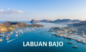 Aerial view of Labuan Bajo harbor with phinisi boats and surrounding hills.